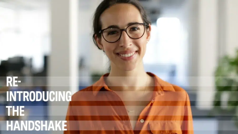 a woman wearing glasses is smiling with the words re introducing the handshake behind her