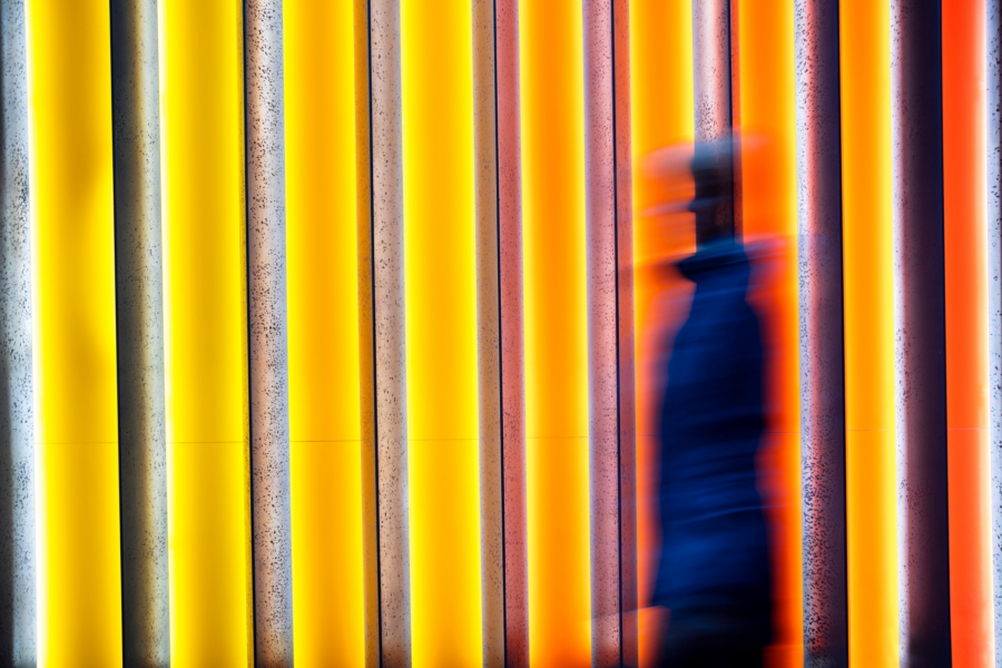 Blurry woman walking past bright, striped lights in a gradient from yellow to orange