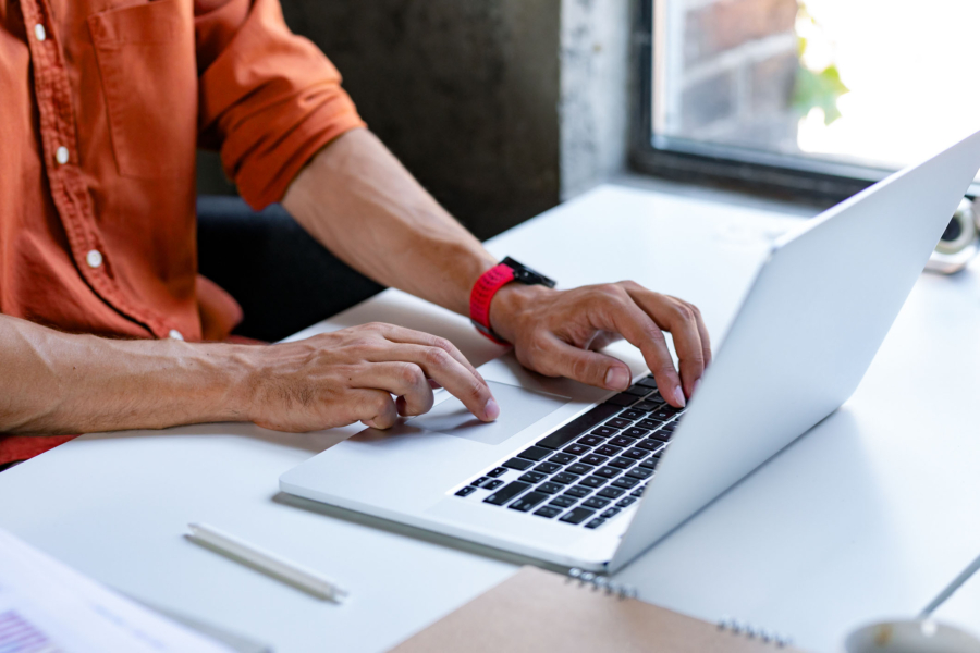 a man wearing a red watch is typing on a laptop