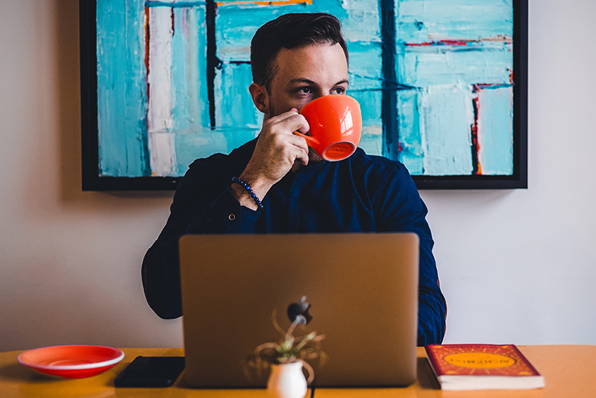 Man drinking orange cup of coffee in front of computer