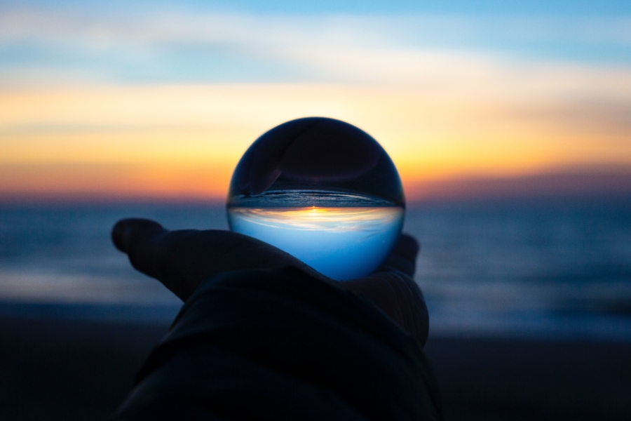 A hand holding a glass ball, view of a beach.