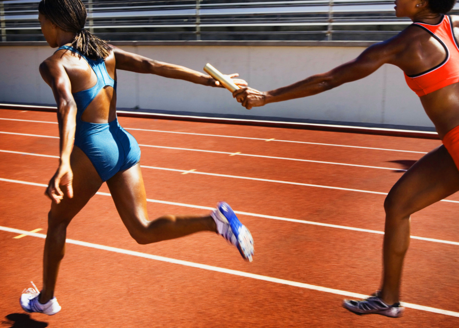 two female runners are passing a baton on a track