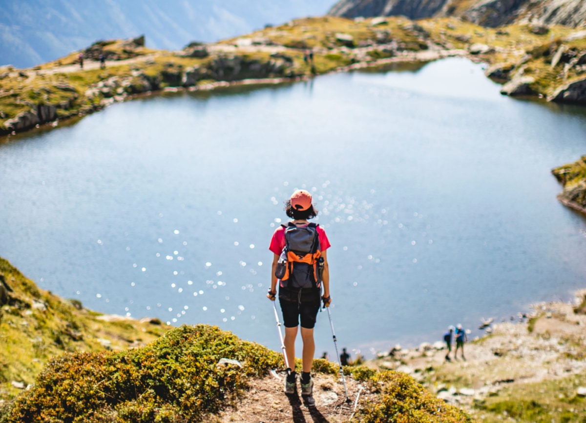a person with a backpack stands on a hill overlooking a lake