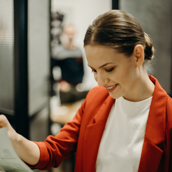 A woman in a red jacket reading a paper.