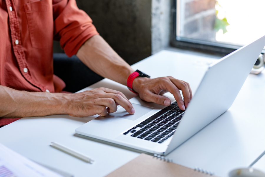 a man wearing a red watch is typing on a laptop