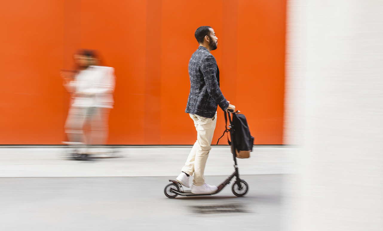 Man with a backpack using an electric scooter.