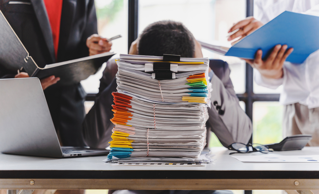 a man sitting at a desk with his head in a pile of papers