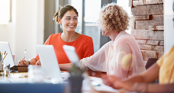 a group of women are sitting around a table with laptops