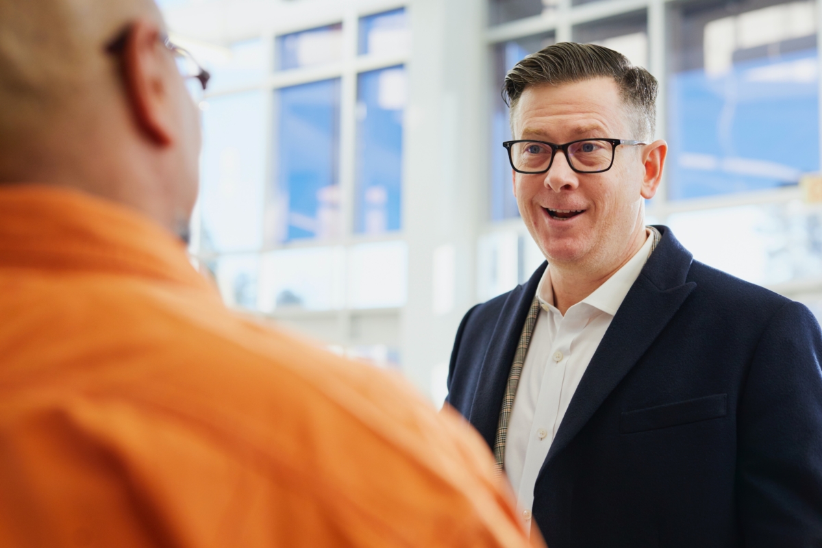 Two men talking. One in a business suit and one in an orange shirt.