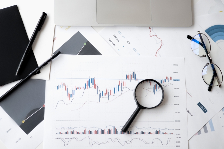 Two pens, glasses, magnifying glass, and a print out of bar chart on a table.