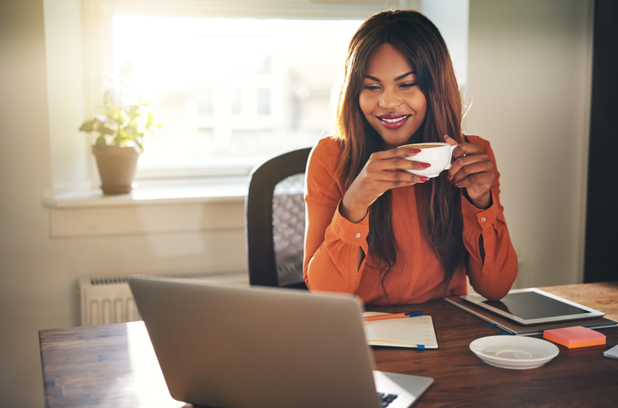 African American woman sipping coffee and smiling in front of a laptop