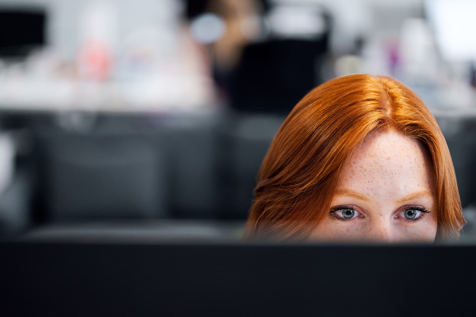 Close up photo of a redhead woman using desktop computer.