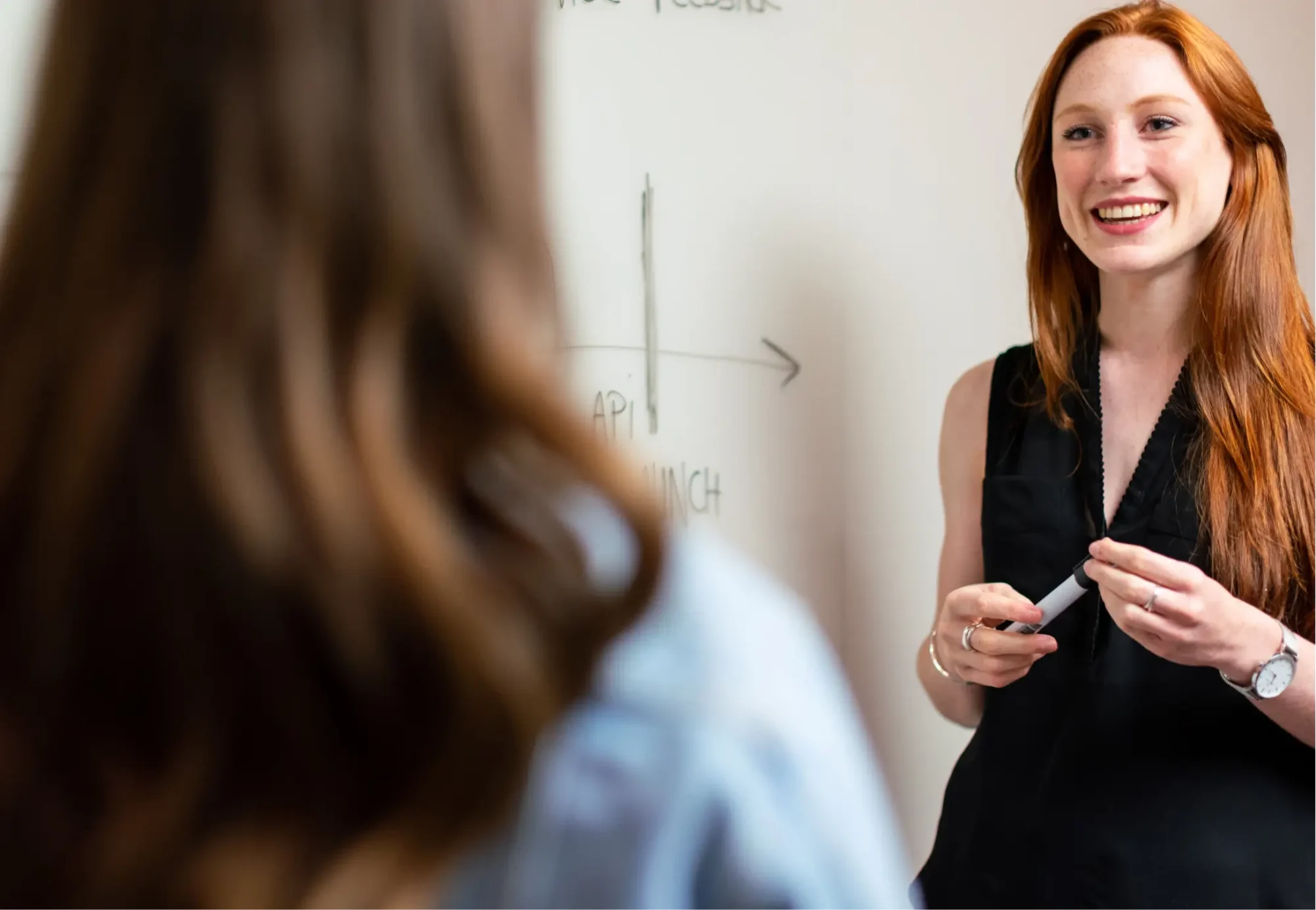 A confident redhead woman in black dress explaining something to her colleague.