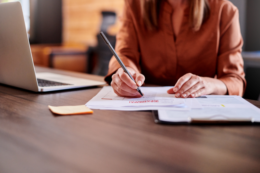 Caucasian woman wearing orange shirt sitting at desk signing a contract